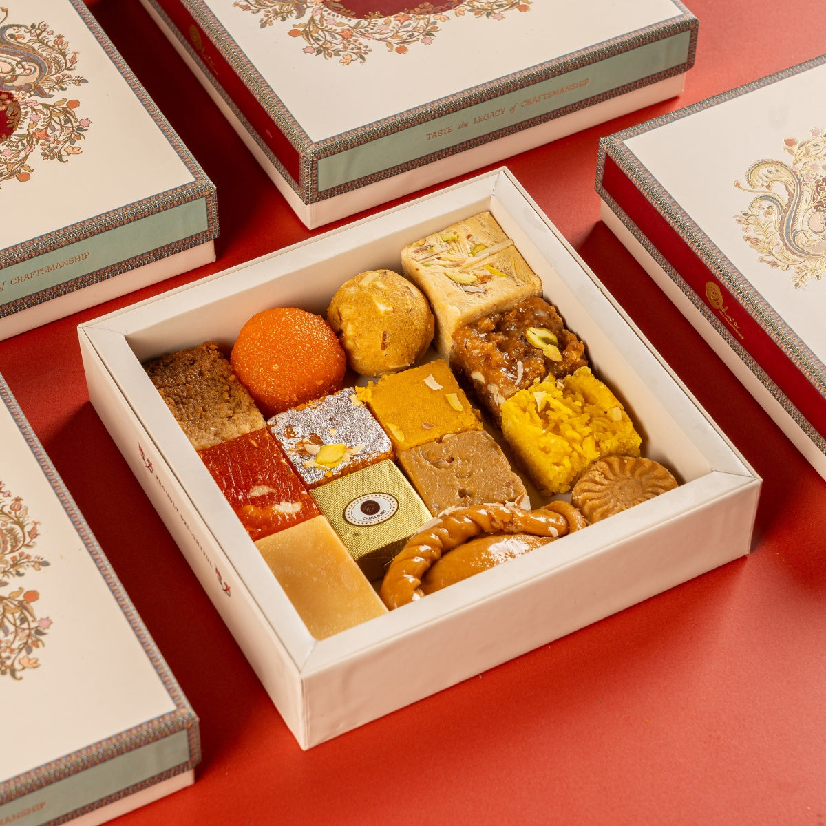 Dadus assorted mithai gift box open, showing eleven traditional Indian sweets including motichoor laddu, sohan papdi, mysore pak and chana burfi, in a cream and gold Diwali presentation box